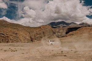 A car kicks up dust while off-roading in the rugged terrain of Spiti Valley.