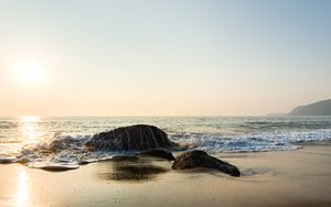 Peaceful beach view with rocks and gentle waves under a warm sunset sky.