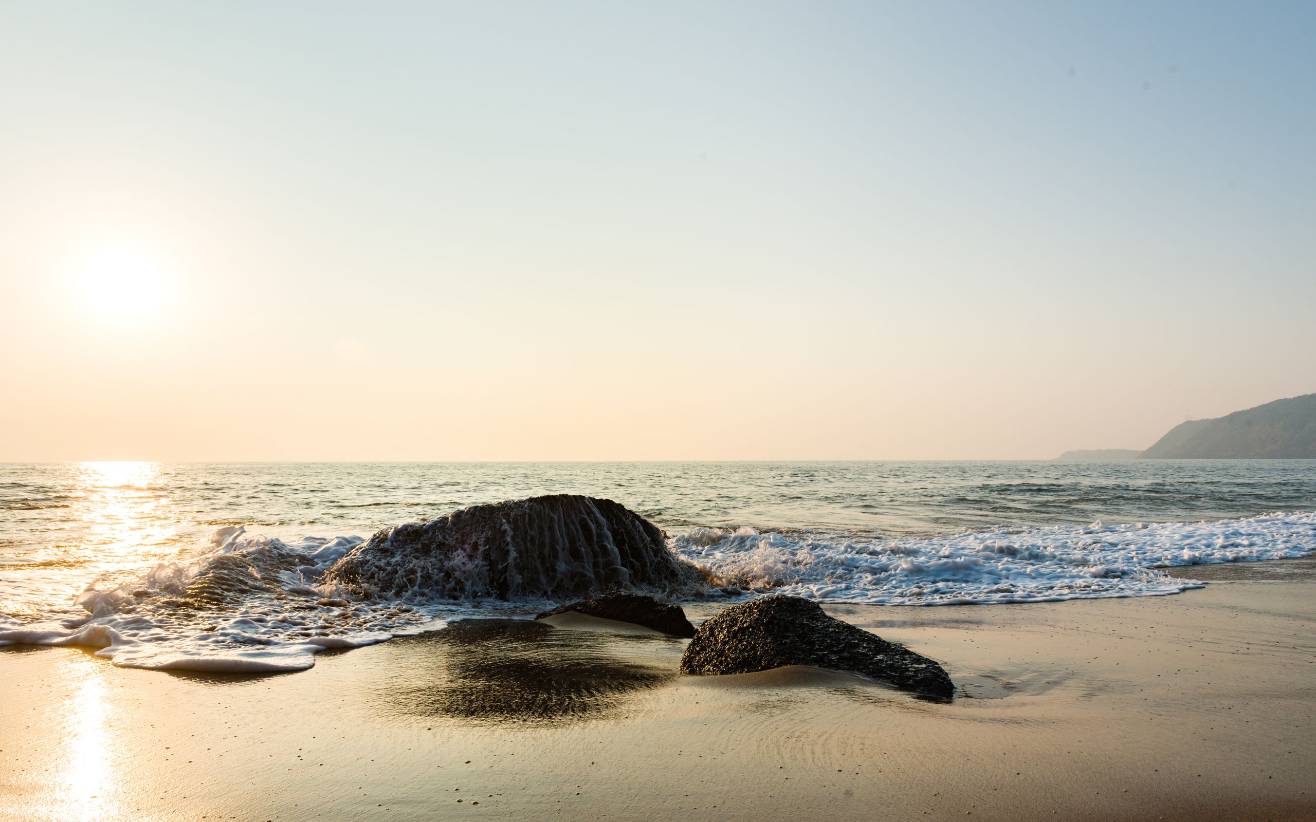 Peaceful beach view with rocks and gentle waves under a warm sunset sky.